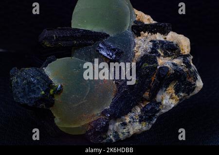Ein Stück von echten grünen Pehnit-Kugeln und dunkelgrünen fast schwarzen Epidot-Spitzen auf Matrix-Makro isoliert auf schwarzer Oberfläche Stockfoto