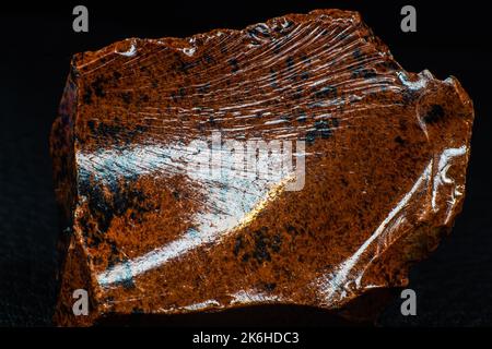 Echtes glänzendes Exemplar eines orangen Mahagoni Obsidian vulkanischen Steinmakros auf schwarzem Lederhintergrund isoliert Stockfoto