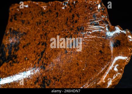 Echtes glänzendes Exemplar eines orangen Mahagoni Obsidian vulkanischen Steinmakros auf schwarzem Lederhintergrund isoliert Stockfoto