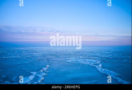 Luftaufnahme des Sonnenuntergangs über dem gefrorenen Meer. Winterlandschaft an der Küste während der Dämmerung. Blick von oben auf das schmelzende Eis im Ozean bei Sonnenaufgang mit Horizont Stockfoto