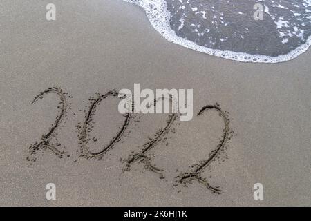 Zahlen von 2022 an der Küste, eine handgeschriebene Nachricht auf dem Sand mit Schaumstoffblasen am Strand. Konzept des ausgehenden Jahres. Stockfoto