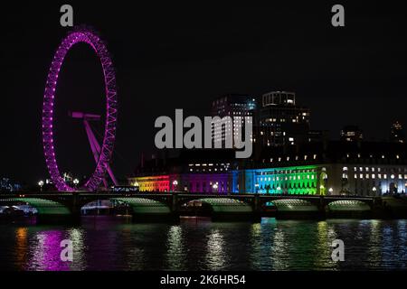 Westminster, London, Großbritannien. 12.. Oktober 2022. Das mit pinkfarbenen Lichtern beleuchtete Londoner Auge reflektiert auf die Themse in Westminster, London. Die County Hall ist auch mit LGBT-Farben des Regenbogens beleuchtet. Kredit: Maureen McLean Stockfoto