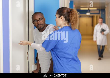 Krankenschwester, die der Patientin beim Gehen hilft, indem sie im Krankenhaus einen Gehhilfe verwendet Stockfoto