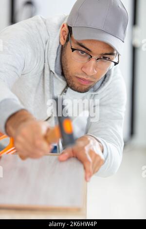 Ein junger Arbeiter, der eine Brille trägt, verwendet einen Hammer Stockfoto