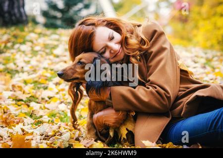 Junge rothaarige Frau posiert im Park mit einem roten Dackel-Hund. Stockfoto