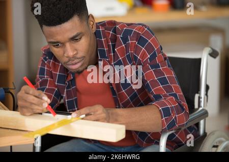 Junger Mann im Rollstuhl versucht sich selbst, sein Bücherregal zu falten Stockfoto