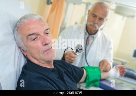 Der Arzt, der den Senior überprüft, bemannt den Blutdruck im Krankenhaus Stockfoto