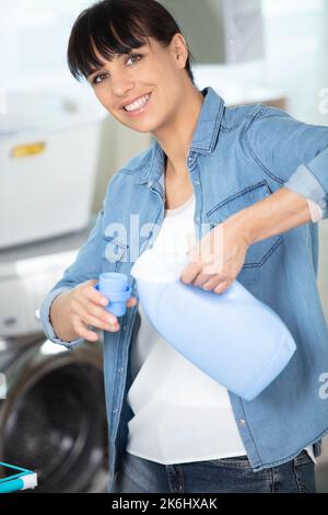 Schöne junge Frau Gießen flüssiges Waschpulver in der Waschmaschine Stockfoto