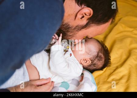 Der junge Vater spielt im Bett und die kleine Tochter im Bett zu Hause. Spaß mit glücklich lächelndem Baby Stockfoto