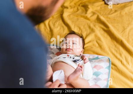 Der junge Vater wechselt zu Hause im Bett die Windel zu einer kleinen Tochter. Alltag in einer modernen Familie Stockfoto