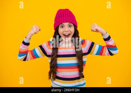 Ein erstaunlicher Teenager. Schöne Winter Kinder Porträt. Teenager Mädchen posiert mit Winter Pullover und Strickmütze auf gelbem Hintergrund. Aufgeregt teen Mädchen Stockfoto