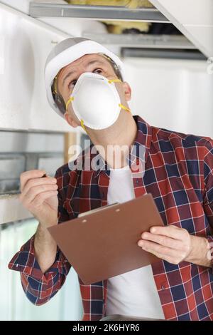 Mann, der auf einer Leiter eine Staubmaske trägt, das Grundstück inspiziert Stockfoto