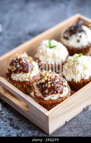 Cupcakes und Muffins in einer Holzkiste. Schokolade und Creme mit Nüssen. Frisch gebackene Süßigkeiten. Stockfoto