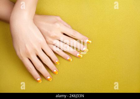 Schöne weibliche Hände mit leuchtend orange Maniküre wie Candy Corn. Gepflegte Nägel mit gelbem Gelpolitur. Halloween-Style Stockfoto