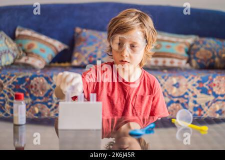 Kind Junge tun chemische Experiment zu Hause. Kinder mit Schutzbrille untersuchen Pipettentropfflüssigkeit in Reagenzgläser, Kaukasisch und Biochemie Stockfoto