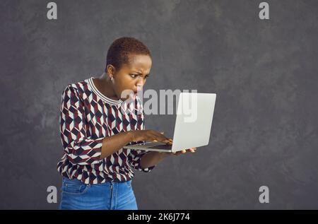 Junge afroamerikanische Frau mit schockiert und überrascht Gesicht Blick auf Laptop-Bildschirm. Stockfoto