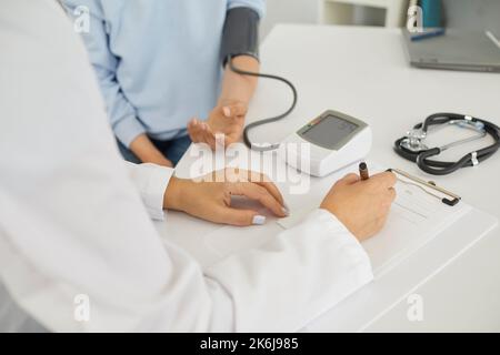 Der Arzt misst den Blutdruck einer jungen Frau mithilfe eines elektronischen digitalen Tonometers. Stockfoto