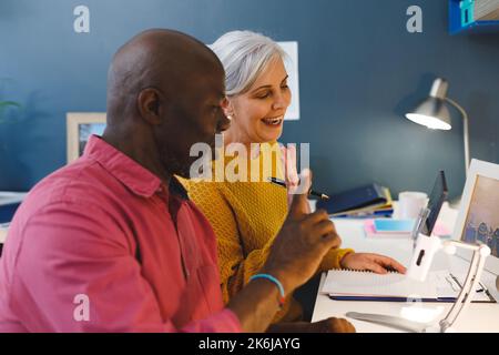 Ein vielseitiges Senior-Paar, das am Tisch sitzt und arbeitet Stockfoto