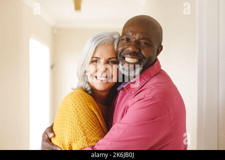 Porträt eines glücklichen, vielfältigen Seniorenpaares, das zu Hause in die Kamera lächelt Stockfoto