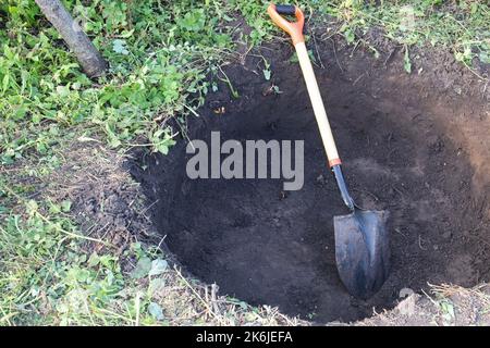 Tiefe Grube im Boden. In der Grube liegt eine Schaufel. Ein Loch gegraben. Stockfoto