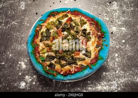 Gebackene Pizza mit Thunfisch, grünem Pfeffer und Käse und blauem Teig. Gesundes Essen, hausgemachte italienische Küche. Farbiger Pizzateig. Stockfoto