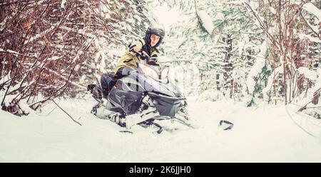 Mann auf dem Schneemobil im Winterberg. Motorschlitten fahren. Mann fährt Schneemobil in verschneiten Wald Stockfoto