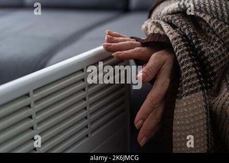 Frau, die sich in Innenräumen in der Nähe des Heizelements die Hände wärmte, Nahaufnahme Stockfoto