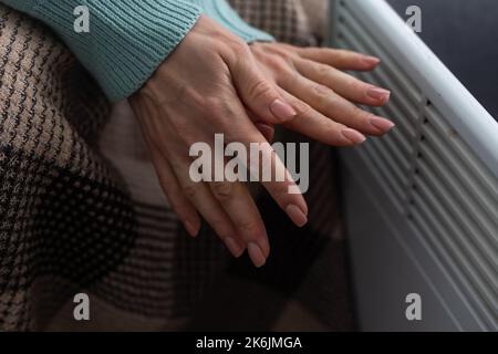 Frau, die sich in Innenräumen in der Nähe des Heizelements die Hände wärmte, Nahaufnahme Stockfoto