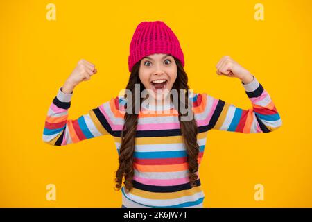 Ein erstaunlicher Teenager. Schöne Winter Kinder Porträt. Teenager Mädchen posiert mit Winter Pullover und Strickmütze auf gelbem Hintergrund. Aufgeregt teen Mädchen. Stockfoto