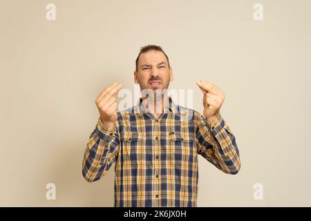 Porträt eines hübschen jungen Mannes mit Bart, der italienische Geste zeigt, was Sie auf beigem Hintergrund möchten. Ein finsterer und düsterer Kerl hat keine Stockfoto