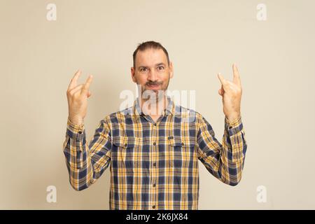 Porträt eines Mannes auf beigem Hintergrund, zeigt eine Geste mit seinen Händen Rock n Roll. Das Konzept der Körpersprache. Stockfoto