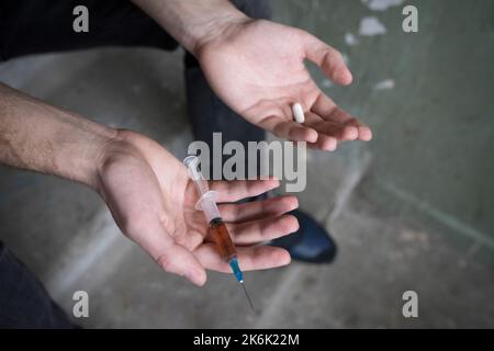 Spritze und Tablette in den Händen eines Süchtigen, Nahaufnahme. Suchtkonzept. Stockfoto