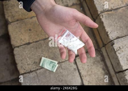 Hand eines Süchtigen, der eine Plastiktüte in seiner Handfläche mit Kokainpulver oder anderen Drogen hält. Nahaufnahme. Suchtkonzept. Stockfoto