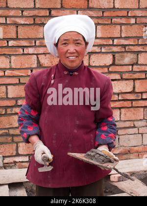Frau / weibliche Ziegelschicht, die die Ziegelsteine eines Gebäudes verlegt / baut die neue Mauer, die in Langmusi, Gansu, China, errichtet wird. VRC. (126) Stockfoto