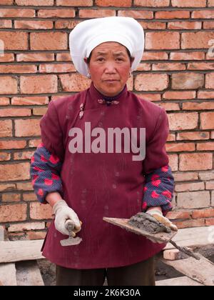 Frau / weibliche Ziegelschicht, die die Ziegelsteine eines Gebäudes verlegt / baut die neue Mauer, die in Langmusi, Gansu, China, errichtet wird. VRC. (126) Stockfoto