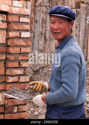 Mann / männliche Ziegelschicht zeigt nach dem Verlegen der Ziegelsteine eines Gebäudes / baut die neue Mauer, die in Langmusi, Gansu, China, gebaut wird. VRC. (126) Stockfoto