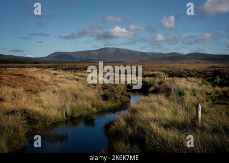 Ein kleiner Bach fließt durch das Moorland von Aughness, Ballycroy, Irland. Am Horizont liegen die Berge des Wild Nephin Nationalparks Stockfoto