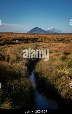 Ein kleiner Bach fließt durch das Moorland von Aughness, Ballycroy, Irland. Am Horizont des Slievemore Berges auf Achill Island Stockfoto