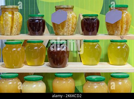 Dunkler und heller Honig in Gläsern auf Holzregalen. Stockfoto