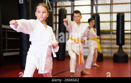 Weibliche Karate-Kämpferin im weißen Kimono, Kampfstellung. Kinder zu zweit üben Karate Stockfoto