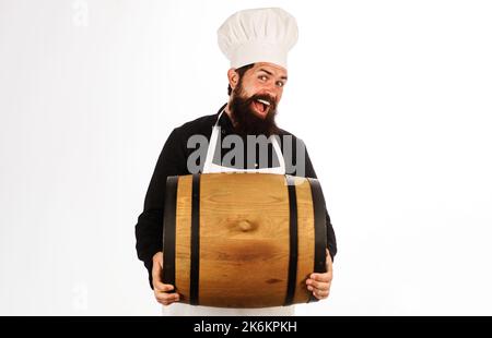 Brauer in der Brauerei mit Holzfass. Oktoberfest. Bärtiger Mann mit Kochhut und Schürze mit Fasswein. Stockfoto