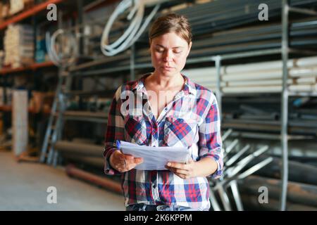 Frau, die im Lager steht und Dokumente in den Händen hält Stockfoto