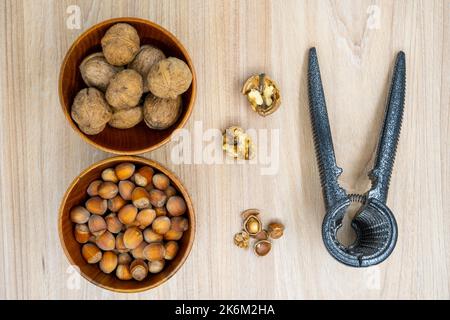 Haselnüsse und Walnüsse in einer Schüssel mit ein paar gerissenen Nussknacker daneben auf dem Tisch. Flach liegend. Stockfoto