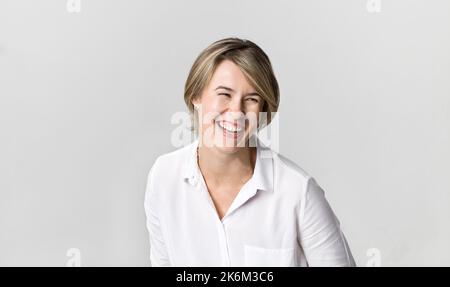 Glückliche junge blonde Frau tragen weiße Hemd lächelt Portrait vor weißem Hintergrund Stockfoto