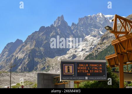 Elektronisches Schild, das die Wartezeit für den Mont-Blanc-Tunnel von Frankreich nach Italien mit dem Mont-Blanc-Massiv im Hintergrund, Courmayeur, warnt Stockfoto