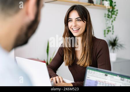 Lächelnde junge Kollegen, die im Büro mit einem Laptop zusammenarbeiten Stockfoto