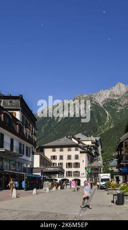 Blick auf die Straße des Stadtzentrums von Chamonix mit Gleitschirmen, die im Sommer über den Berg Le Brevent fliegen, Haute Savoie, Frankreich Stockfoto