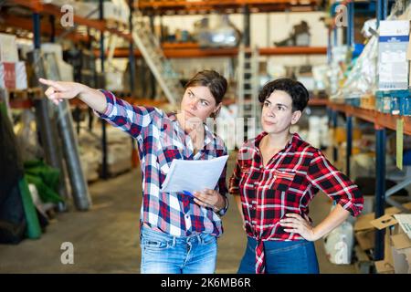 Der Manager sprach mit einer Mitarbeiterin im Lager und zeigte mit der Hand auf die Schachteln mit Produkten Stockfoto
