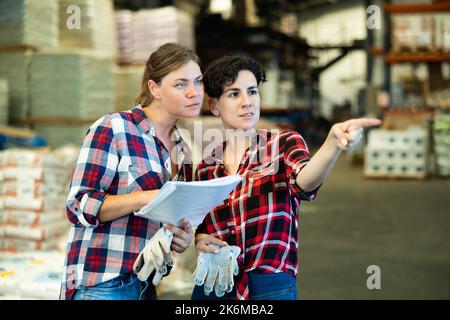 Der Manager sprach mit einer Mitarbeiterin im Lager und zeigte mit der Hand auf die Schachteln mit Produkten Stockfoto
