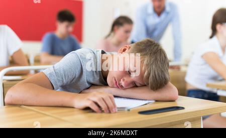 Gelangweilter Teenager, der während des Unterrichts am Schreibtisch im Klassenzimmer schläft Stockfoto